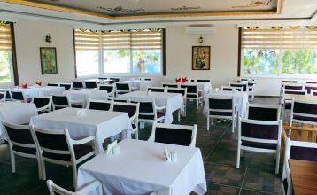The Linda Resort is a multi-story hotel overlooking an outdoor pool equipped with lounge chairs, umbrellas, and palm trees under a bright blue sky.