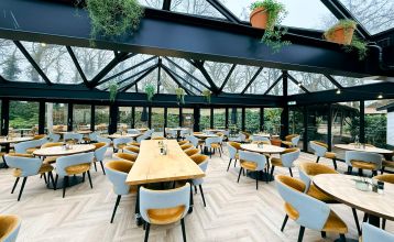 Hotel De Beyaerd’s bright, modern restaurant features large glass walls, light wood floors, and stylish gray and yellow chairs—an ideal setting for teambuilding activities surrounded by lush greenery.