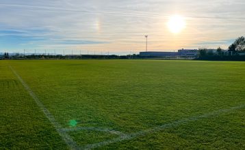 The four-story Hotel Plaza Inn Wiener Neustadt has a modern white exterior, glass lobby doors and an overhang of parked cars at sunset, just steps away from a modern training facility in Wiener Neustadt.