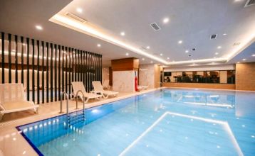 The Side Moon Palace is a modern hotel with several floors and balconies from which guests can enjoy a view of a spacious outdoor pool lined with rows of white lounge chairs and closed umbrellas.