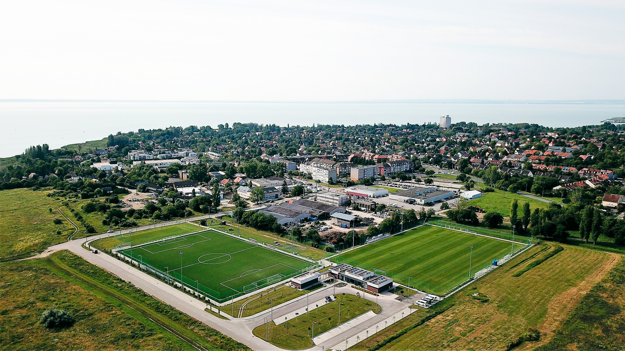 Modern football facility in Hungary, located directly on Lake Balaton, with artificial turf pitch and solar panels on the club building.