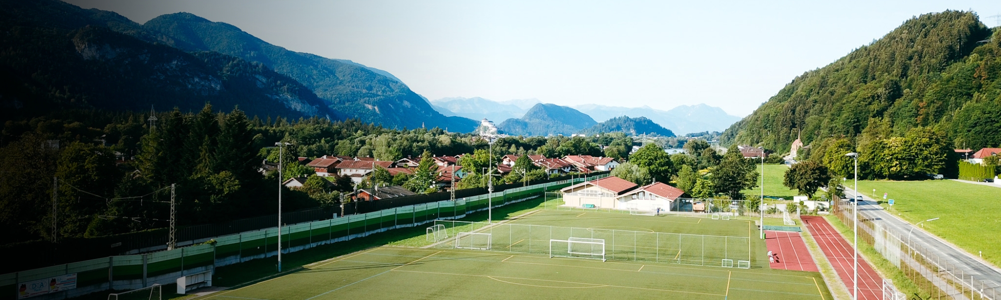Fußballplatz in Bayern, umgeben von Bergen und grüner Natur, mit Blick auf ein Dorf im Tal.