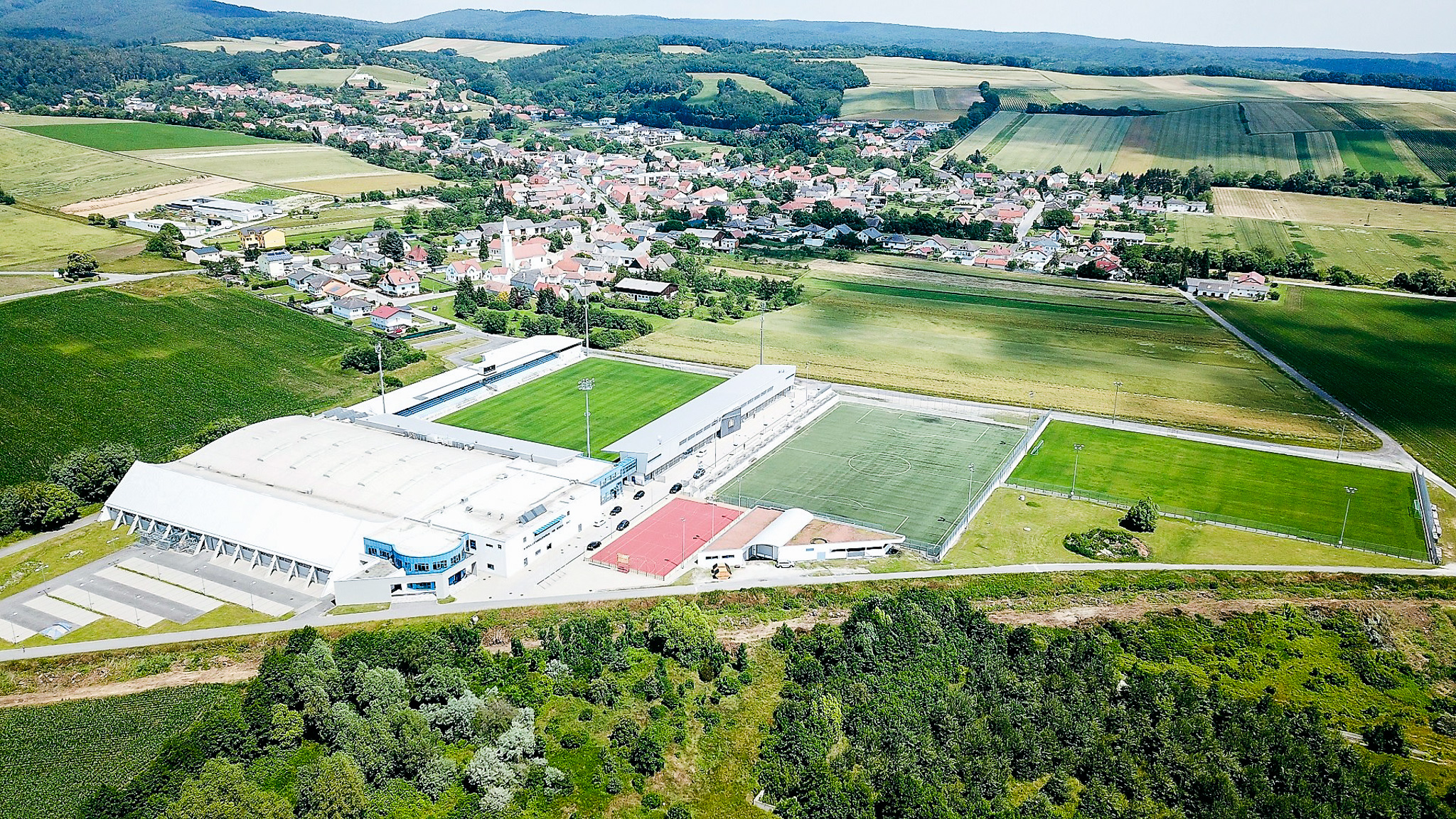 Weitläufige Fußballtrainingsanlage im Burgenland mit Rasenplätzen, Kunstrasenplatz, Sporthalle und umliegenden Feldern in ländlicher Idylle.