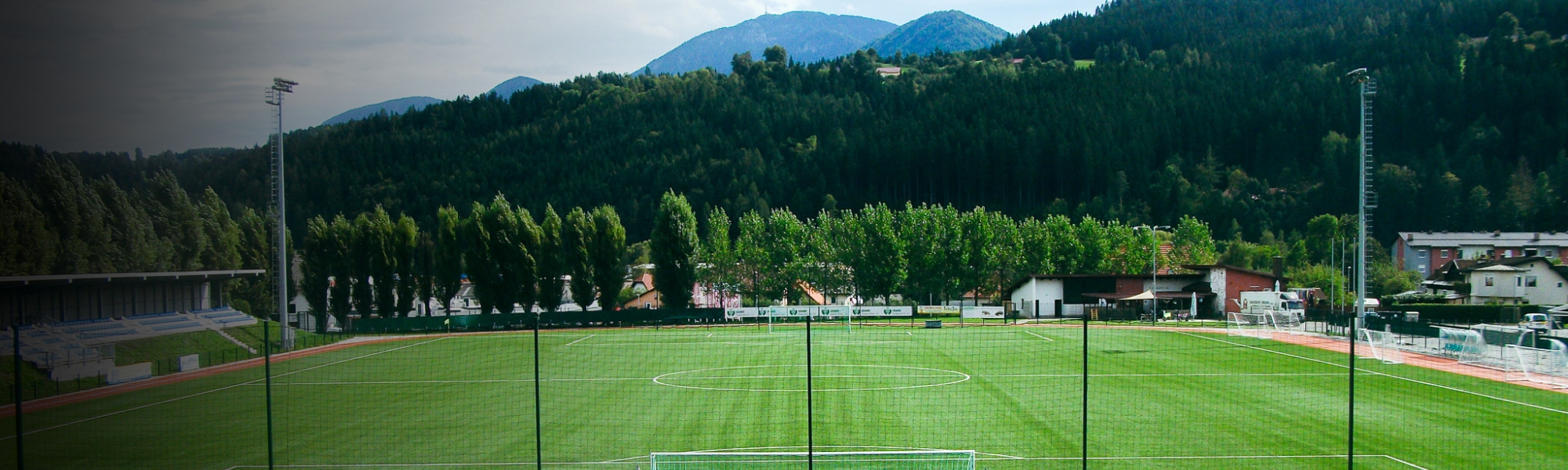 Football pitch in Carinthia, surrounded by green forests and mountain scenery, with modern stands and floodlights.