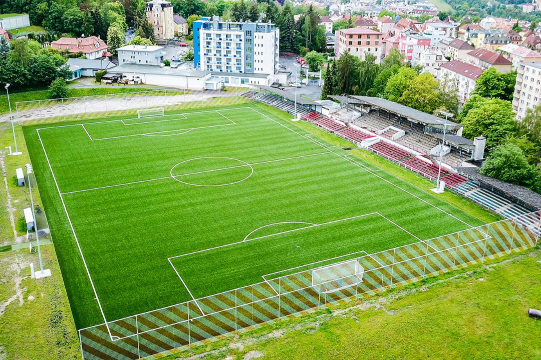  Fußballstadion mit Tribünen, umgeben von einer hügeligen Stadtlandschaft mit vielen Bäumen.