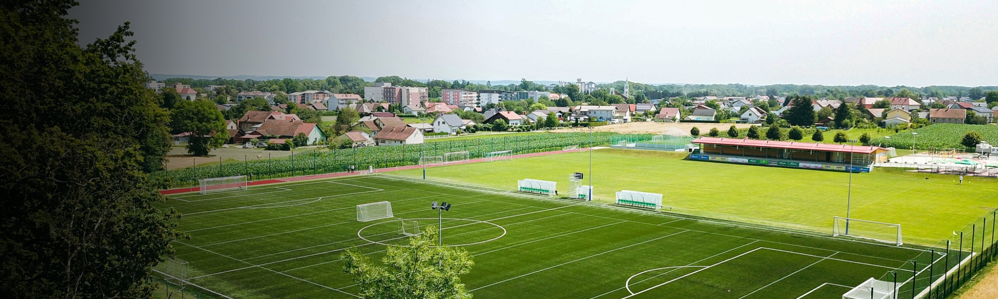 Fußballtrainingslager mit Kunstrasen- und Naturrasenplatz inmitten einer idyllischen Landschaft mit kleinen Häusern im Hintergrund.