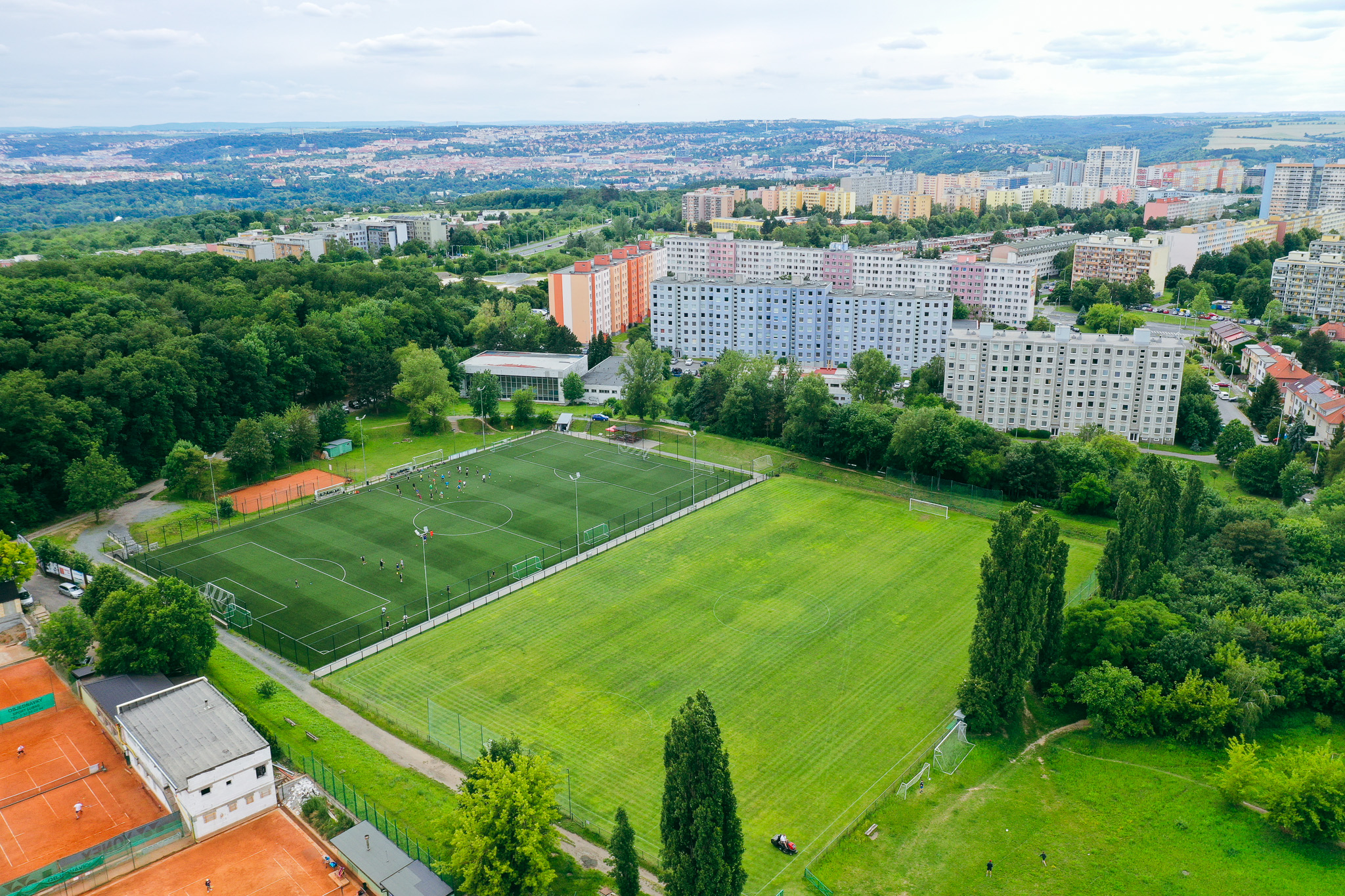 Football pitch in the middle of a green landscape with a view of a city with many tower blocks.