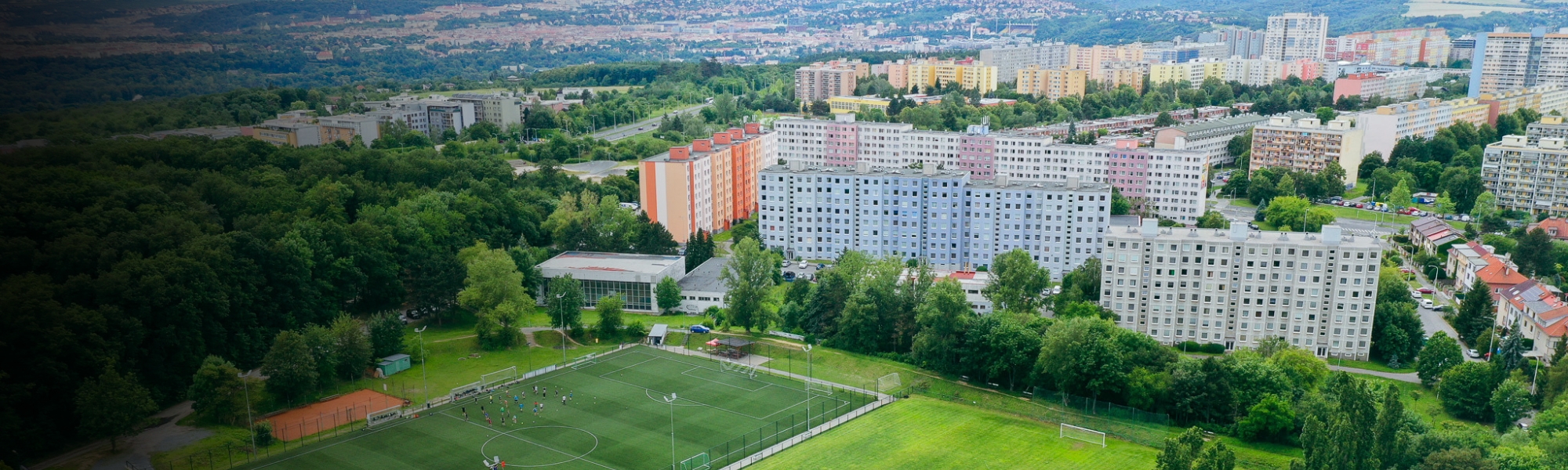 Fußballplatz inmitten einer grünen Landschaft mit Blick auf eine Stadt mit vielen Hochhäusern.