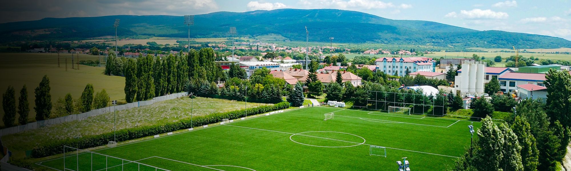 Fußballtrainingsanlage in der Slowakei, eingebettet in eine Kleinstadtlandschaft mit Bergen im Hintergrund und Flutlichtmasten auf dem Platz.