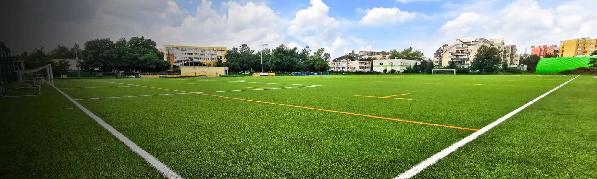 Moderner Kunstrasenplatz mit klaren Spielfeldmarkierungen, umgeben von Wohngebäuden und Sporteinrichtungen.