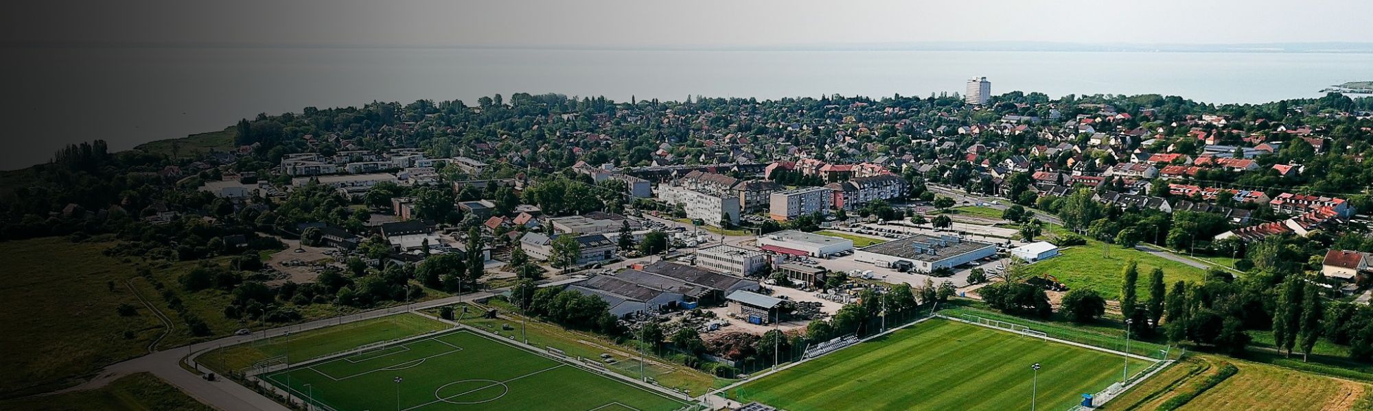 Fußballtrainingsplatz in Ungarn mit Blick auf den Balaton, umgeben von Bäumen und Werftanlagen am See.