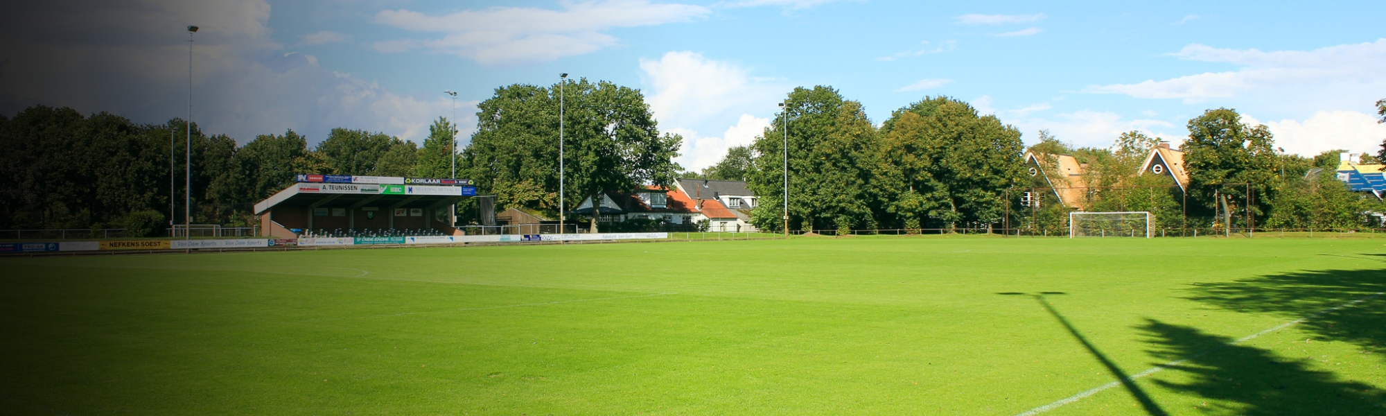 Football pitch in Utrecht, taken from a different perspective, with stands, goals and surrounding houses and trees in the background.