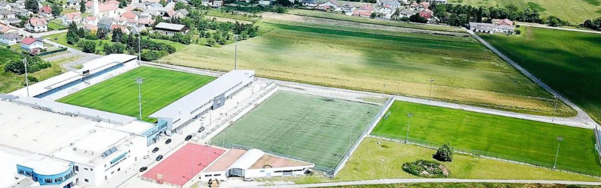 Luchtfoto van een sportcentrum in Burgenland, omringd door groene velden en een klein dorp met rode daken.