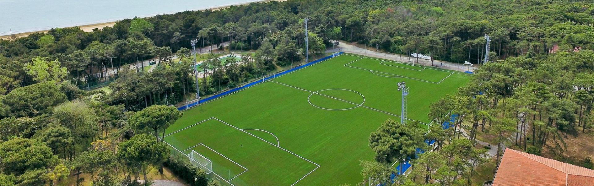 Voetbalcomplex aan de Boven-Adriatische Zee met een kunstgrasveld, omgeven door bomen en vlak bij het strand