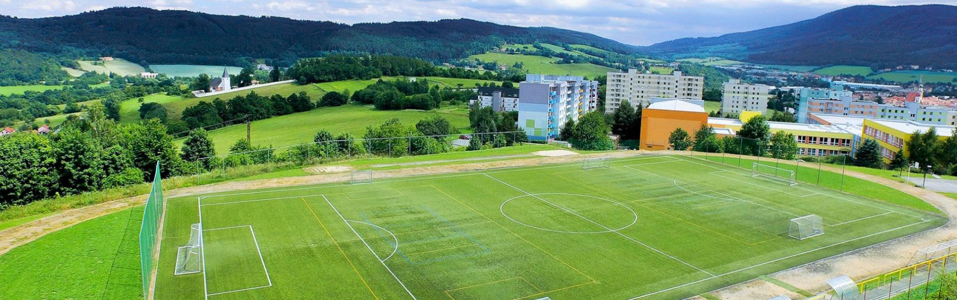  Voetbalveld met kunstgras in een schilderachtig heuvellandschap, omringd door woonhuizen.