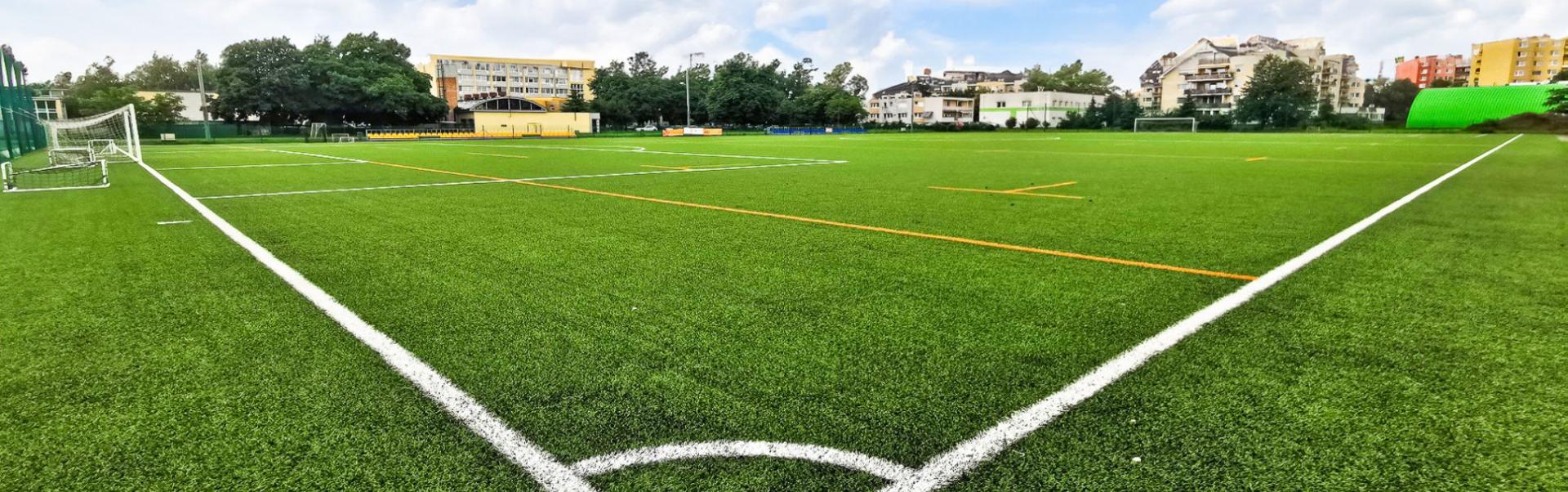 Modern kunstgrasveld met duidelijke veldmarkeringen, omringd door woongebouwen en sportfaciliteiten.