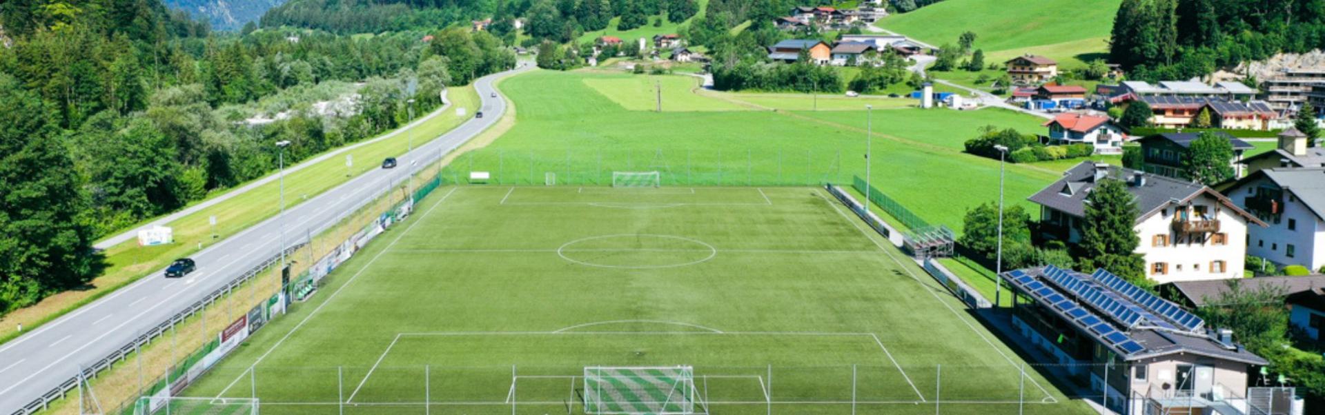 Panoramisch uitzicht op een voetbalveld met een klein dorp en bergen in Oostenrijk op de achtergrond.