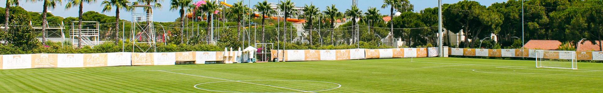 Perfect voetbalveld in Belek, omringd door palmbomen en schijnwerpers.