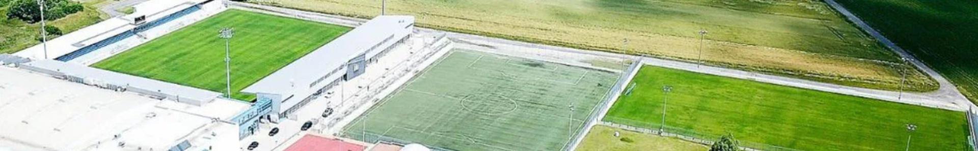 Ruime voetbaltrainingsfaciliteit in Burgenland met grasvelden, kunstgrasveld, sporthal en omliggende velden in een idyllische landelijke omgeving.