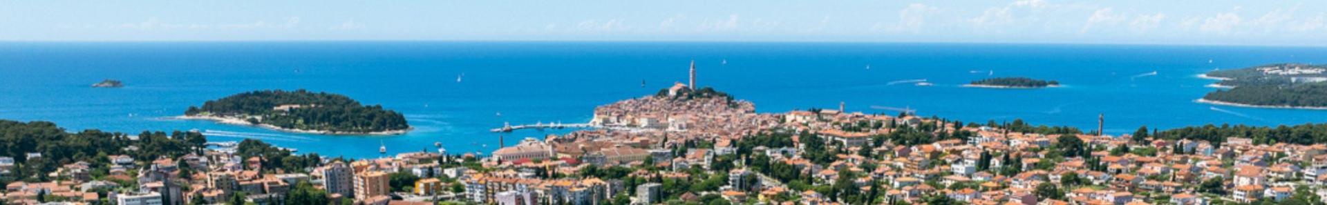Luchtfoto van een voetbaltrainingscentrum in Kroati&euml; met verschillende gras- en kunstgrasvelden, schijnwerpermasten, omgeven door woongebouwen en groene zones, met een kleine stad en de Adriatische Zee op de achtergrond.