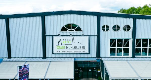 Hotel Stadt Mühlhausen*** is een groot, modern, grijs-wit gebouw met ronde ramen, een bord boven de ingang, bomen in de buurt, een bewolkte hemel en een eigen fitnessruimte voor het comfort van de gasten.