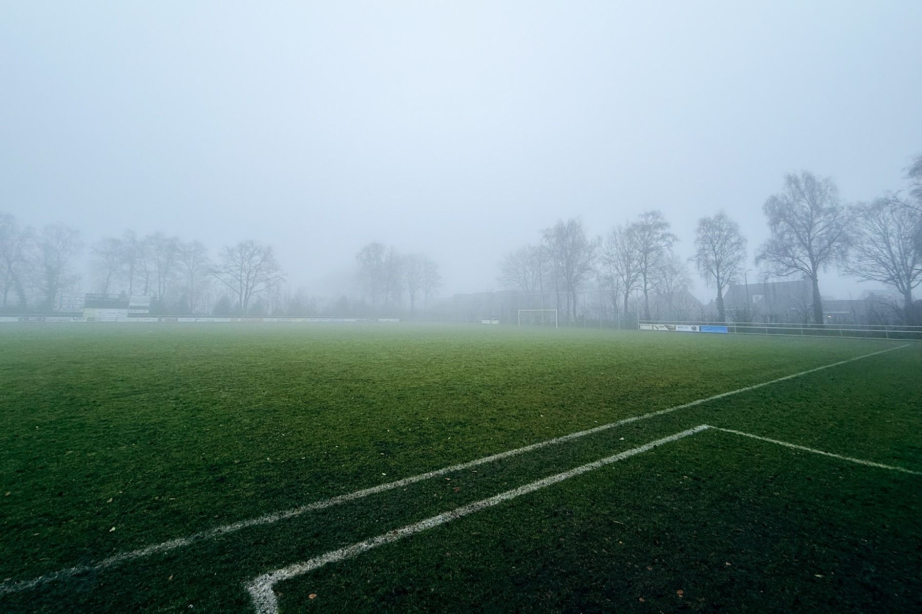 Ein nebliger Fußballplatz am Sporthotel Bruurs, mit kaum sichtbaren weißen Linien und nebelverhangenen Bäumen - ein idealer Ort in Baarle-Nassau für Trainingslager am frühen Morgen.