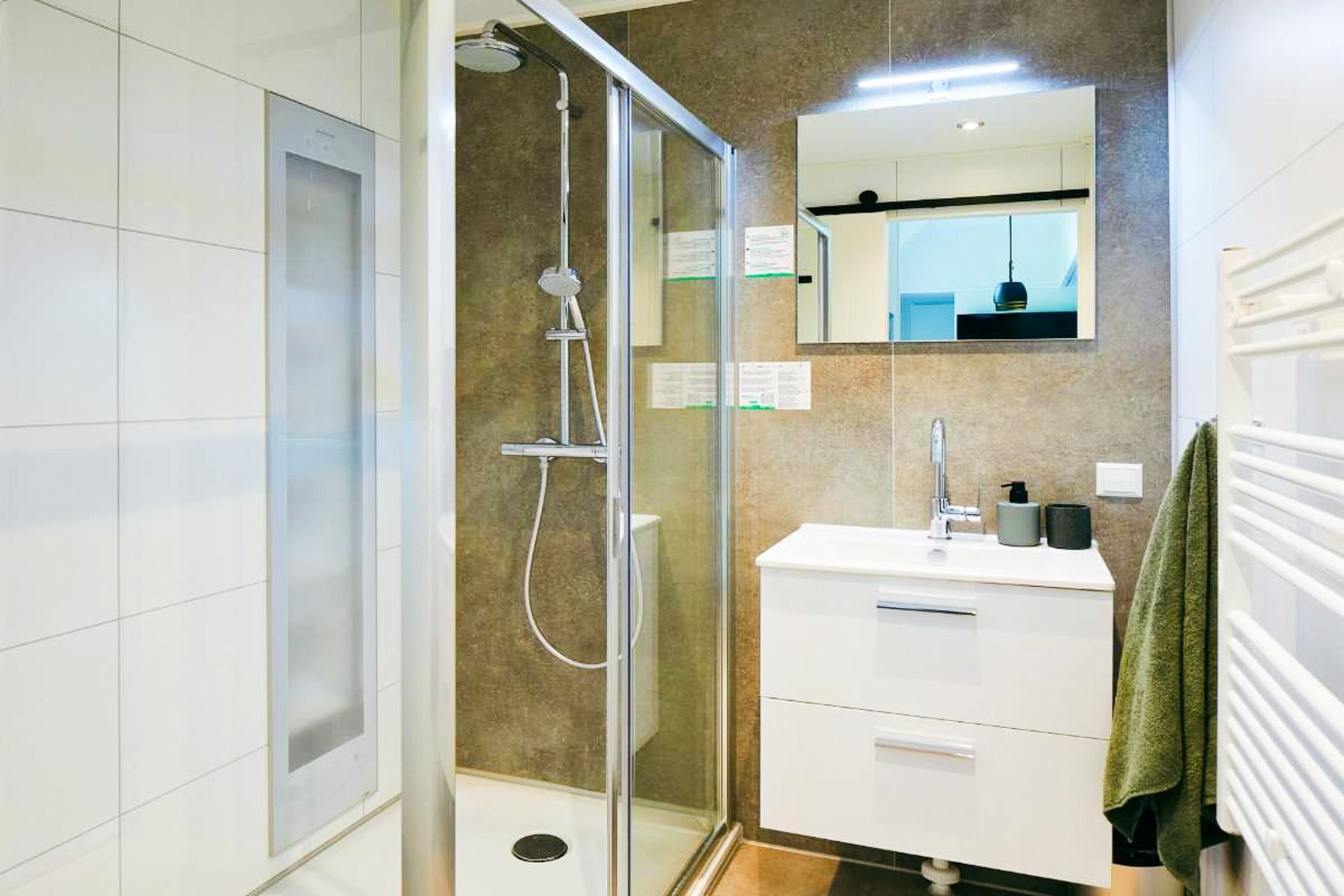 Moderne badkamer met glazen douche, regendouchekop, wit wastafelmeubel met lades, wandspiegel en handdoek aan de zijkant - perfect om te ontspannen na een dagje Duinrell of een intensief voetbaltrainingskamp.