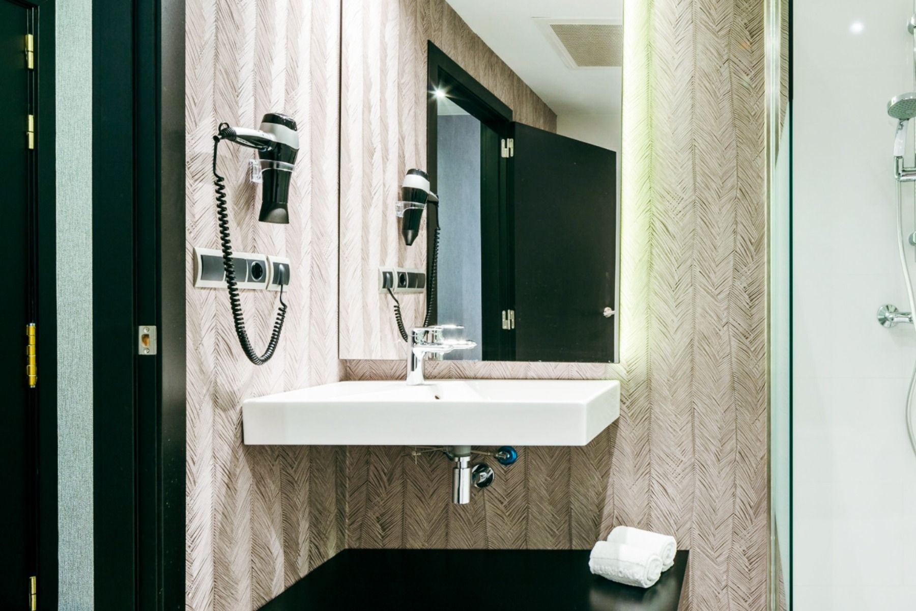 Moderne bad på Hotel ILUNION Bel Art Barcelona med hvit vask, veggmontert hårføner, stort speil, brettede håndklær og dusjkabinett i glass. Stilige, mønstrede vegger gir en moderne stil inspirert av lokale treningsfasiliteter.