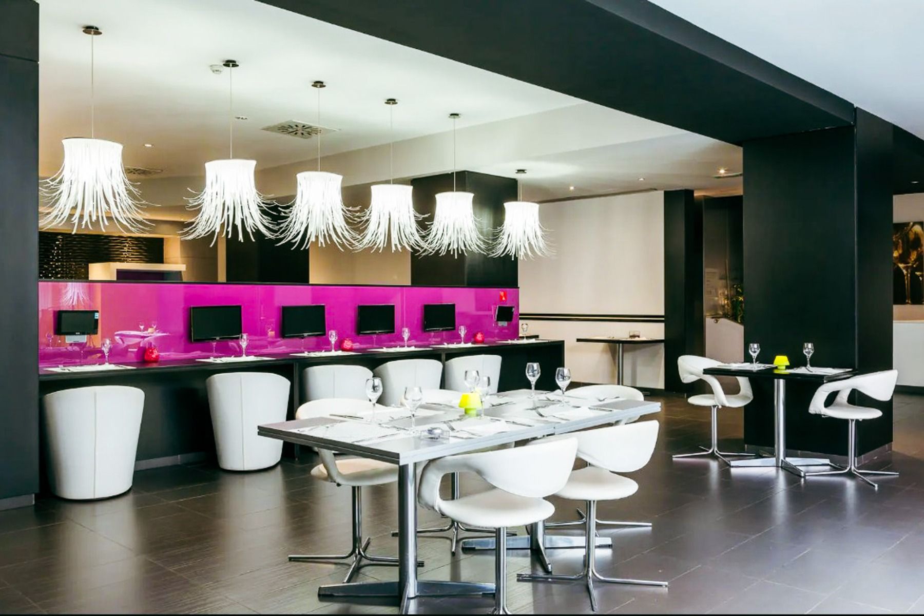 En moderne restaurant på Hotel ILUNION Bel Art Barcelona har hvite stoler, mørke bord, unik lysekronebelysning, datamaskiner på en disk og en levende rosa glasskillevegg som fanger opp den dynamiske stemningen i Fußballkultur Barcelona.