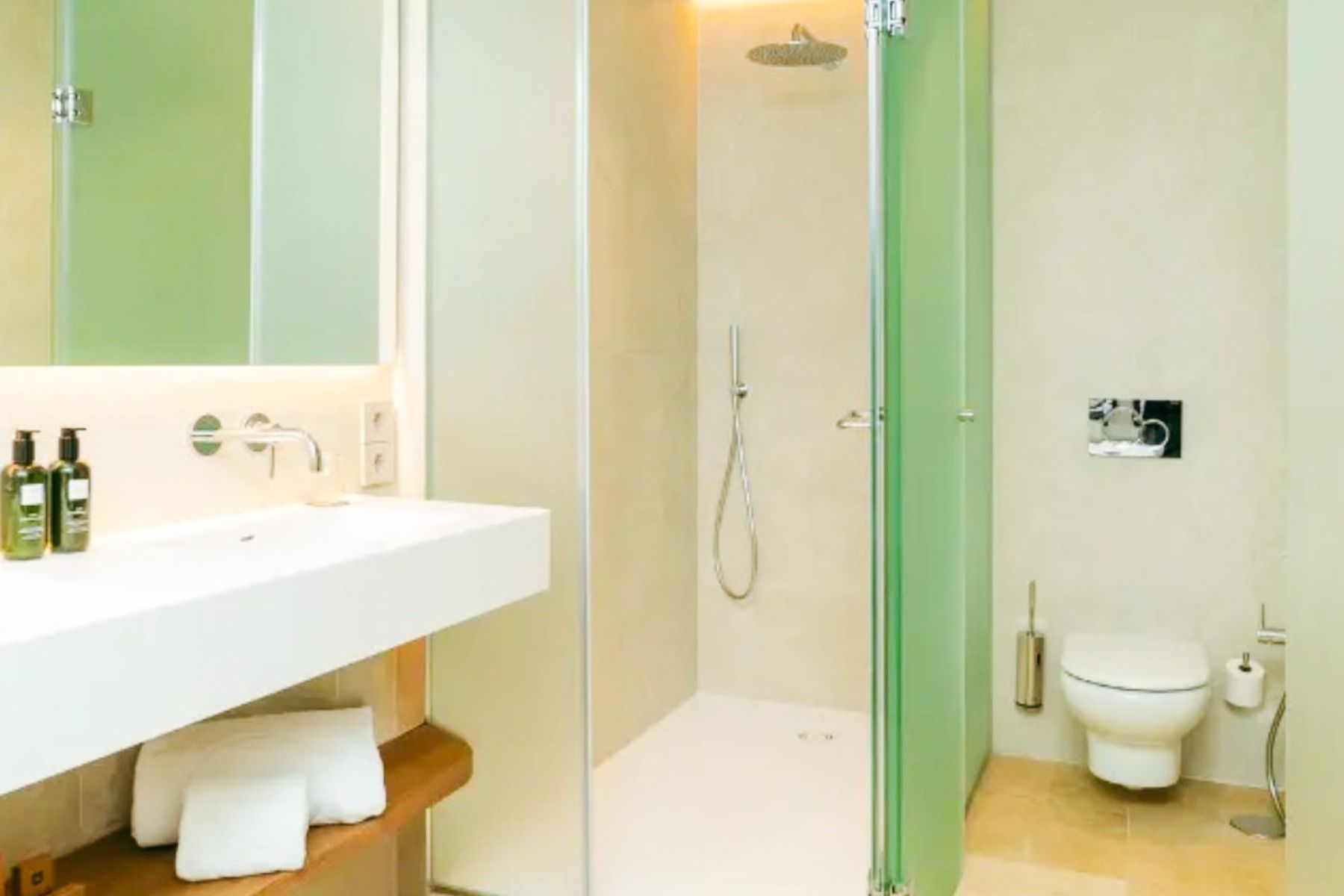 Een moderne badkamer in het SH Villa Gadea* Hotel met een glazen douchecabine, een wandhangend toilet, een vrijstaande wastafel, toiletartikelen, handdoeken op een houten plank en een minimalistische, neutrale inrichting – ideaal voor voetbalteams tijdens