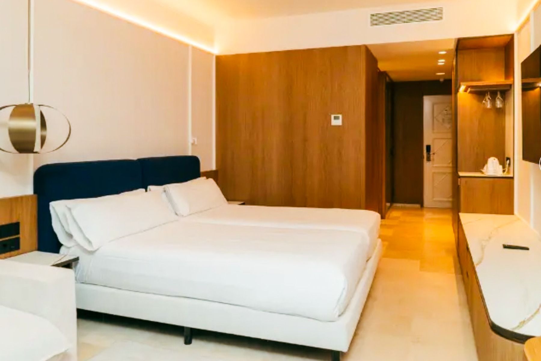 Een moderne kamer in Hotel SH Villa Gadea* is voorzien van twee nette bedden, houten accenten, een wandspiegel, een lang aanrechtblad en sfeervolle verlichting – perfect voor voetbalteams tijdens hun trainingskamp in Altea.