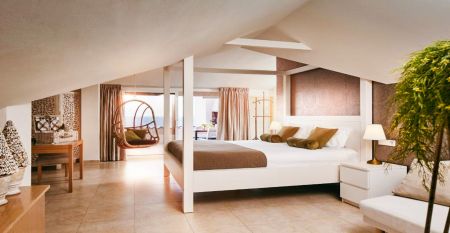 Het Van der Valk Hotel BARCAROLA is een 4-sterrenhotel in mediterrane stijl aan de Costa Brava met balkons met vlaggen, een helderblauw zwembad, pooltafels met parasols en palmbomen onder een helderblauwe hemel.