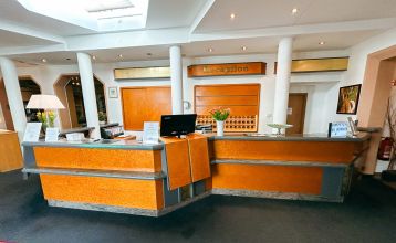 Hotel Empfinger Hof, med rødt tegltak og kvistevinduer, ønsker gjester velkommen til Fußballtrainingslager. Et "Hotel Restaurant"-skilt kroner bygningen, med trær og en asfaltert inngang som tilbyr gute Verpflegung og solrik varme.