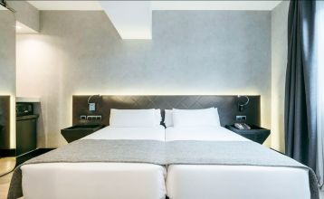 Inngangen til Hotel ILUNION Bel Art Barcelona har store glassdører, potteplanter og et skilt over den svarte markisen - perfekt for gjester som vil utforske Fußballkultur Barcelona eller besøke Trainingseinrichtungen i nærheten.