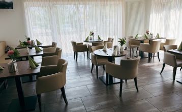 Luchtfoto van Hotel Drei Rosen in Moosburg an der Isar — een vier verdiepingen tellend, lichtpaars hotel met zonnepanelen, glazen balkons en een buitenterras met oranje tafels en stoelen, ideaal voor een voetbaltrainingskamp.
