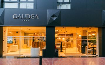 Buitenaanzicht van Hotel Gaudea met grote glazen ramen die een helder verlichte, stijlvolle lobby en bar tonen - op slechts een paar minuten van het strand van Santa Pola.