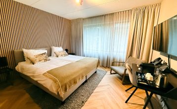 Hotel De Beyaerd biedt een ruim, modern restaurant met grote glazen ramen, lichthouten tafels, grijze en mosterdkleurige stoelen, hangende potplanten en uitzicht op bomen - ideaal voor teambuildingsactiviteiten.