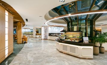 Luchtfoto van het Limak Arcadia Hotel met zwembaden, tuinen, sportvelden en strandcabines - ideaal voor het voetbaltrainingskamp Turkije - omringd door palmbomen en bergen onder een heldere hemel.