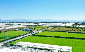 Luchtfoto van het Limak Arcadia Hotel met zwembaden, tuinen, sportvelden en strandcabines - ideaal voor het voetbaltrainingskamp Turkije - omringd door palmbomen en bergen onder een heldere hemel.