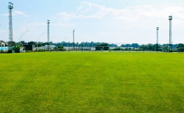 Luchtfoto van het Limak Arcadia Hotel met zwembaden, tuinen, sportvelden en strandcabines - ideaal voor het voetbaltrainingskamp Turkije - omringd door palmbomen en bergen onder een heldere hemel.