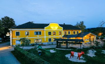 Een knalgeel gebouw in Neuhofen an der Ybbs met een steiger, ladder en zwarte opblaasboot ligt aan een rustige vijver op het platteland - mensen genieten van dit tafereel in het door een familie gerunde Hotel Perbersdorfer Heuriger.