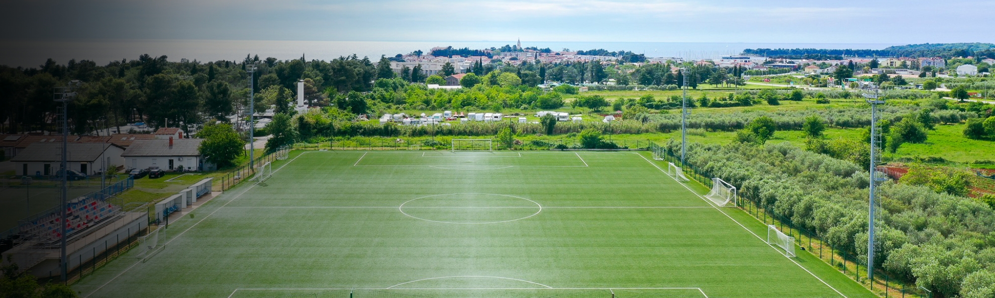 Panoramische opname van een voetbalveld met kunstgras in Istrië, omlijst door olijfgaarden en mediterraan landschap, met uitzicht op de kust en de stad Poreč.