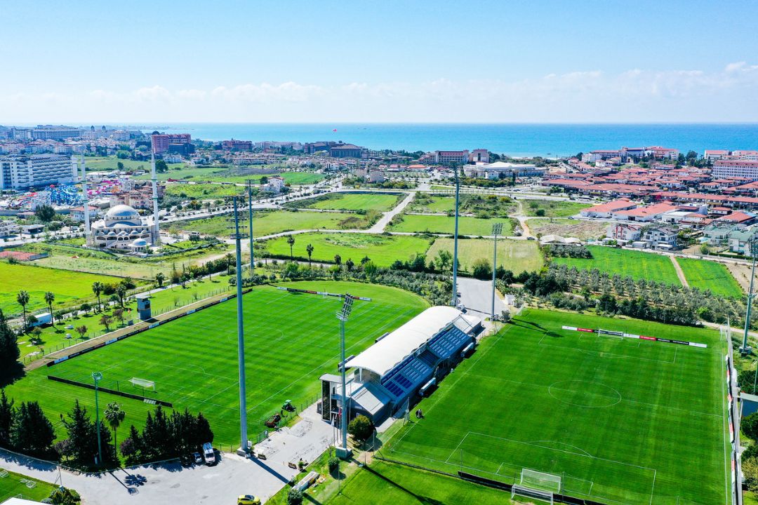 Voetbaltrainingskamp in Turkije met twee goed onderhouden voetbalvelden, omgeven door groene natuur en dicht bij de kust.