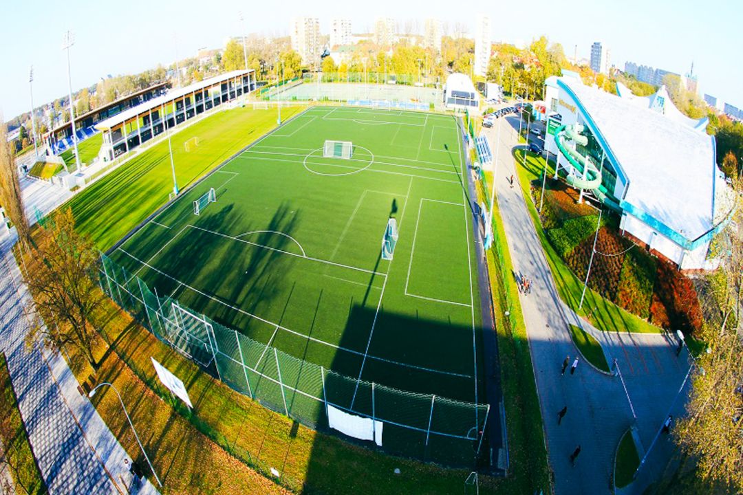 Luftaufnahme eines modernen Fußballtrainingsgeländes mit mehreren Spielfeldern, Tribünen und einer angrenzenden Sporthalle