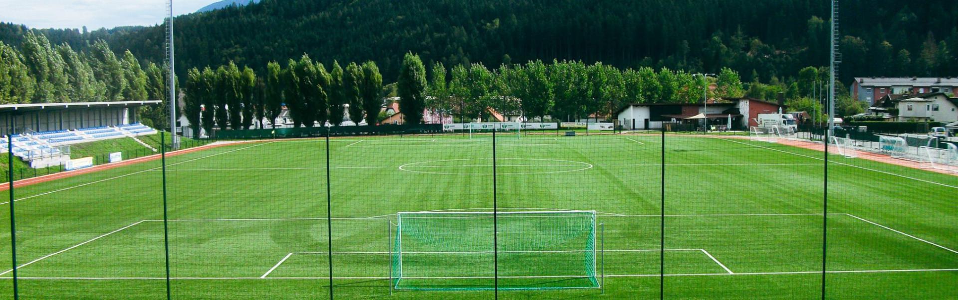 Fotballbane i K&auml;rnten, omgitt av en idyllisk alpin natur med tribune og treningsfasiliteter.
