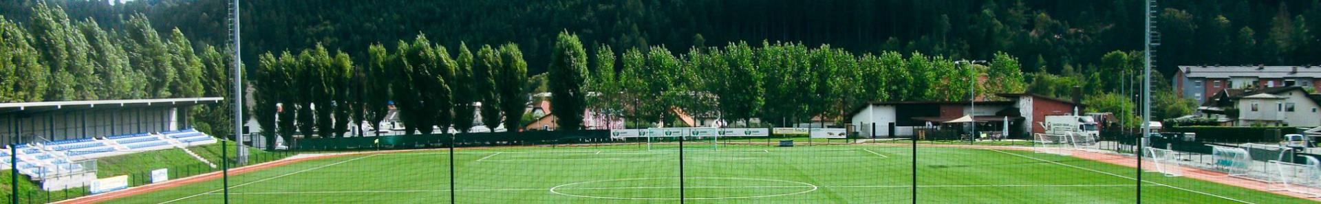 Fotballbane i K&auml;rnten, omgitt av en idyllisk alpin natur med tribune og treningsfasiliteter.