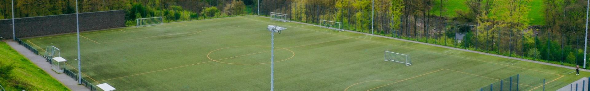 Luftfoto av en moderne fotballbane med kunstgress i Nordrhein-Westfalen, omgitt av gr&oslash;nne &aring;ser og landlig natur.