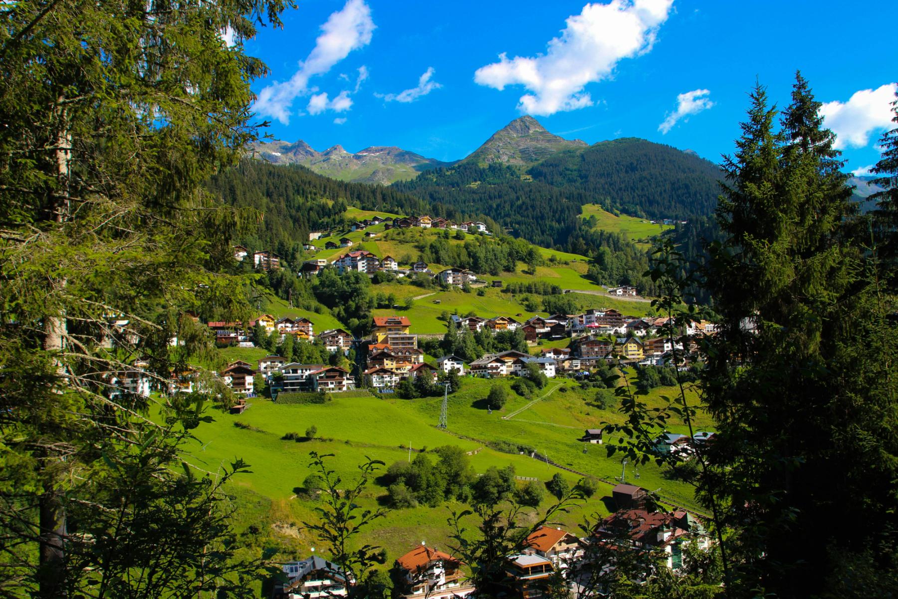 Malerisches Bergdorf in &Ouml;sterreich, umgeben von gr&uuml;nen Wiesen, W&auml;ldern und Bergen unter blauem Himmel