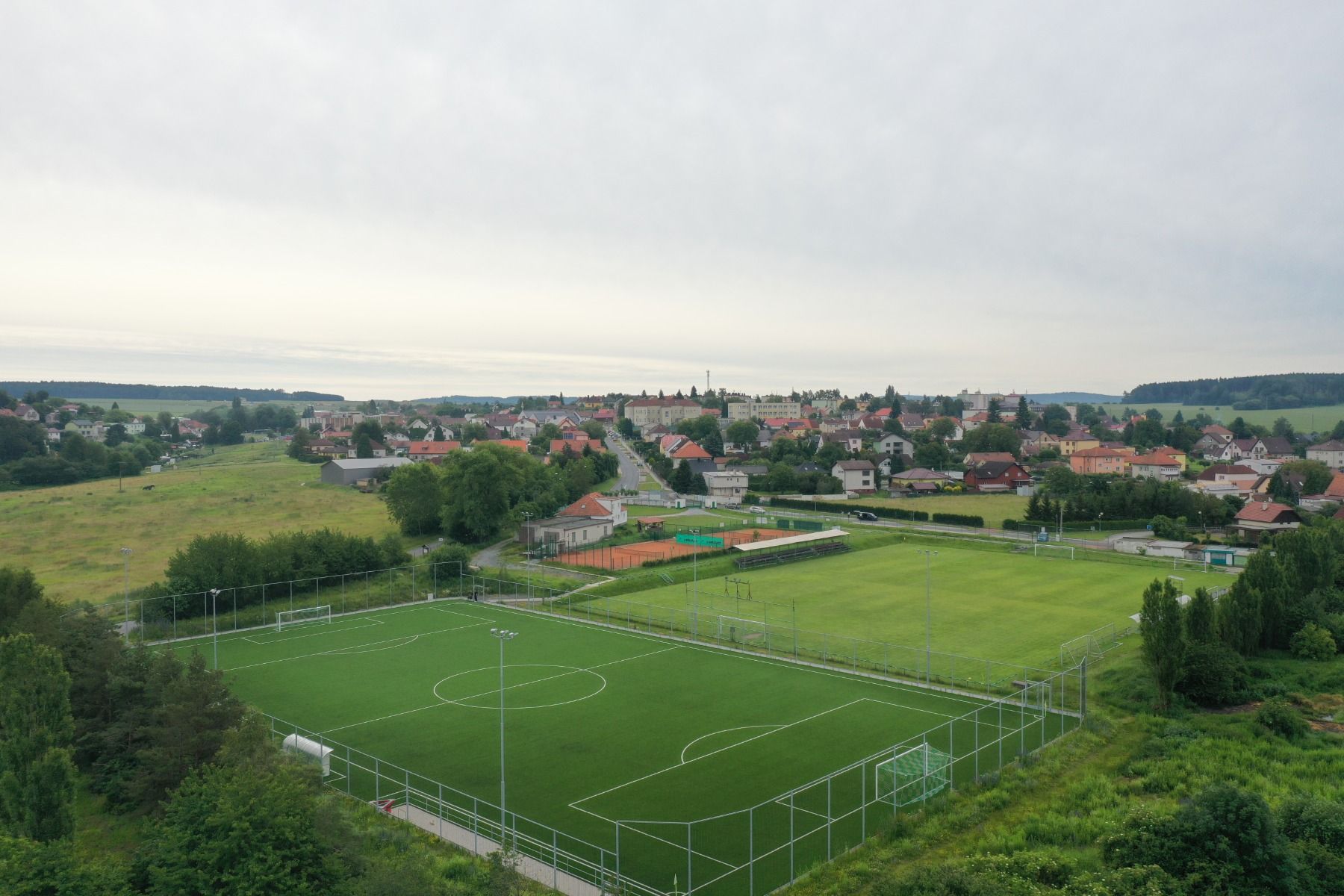 Luftaufnahme eines grünen Fußballplatzes mit weißen Markierungen in der Nähe einer kleinen Stadt, zwischen Häusern und Bäumen unter bewölktem Himmel - nur wenige Schritte vom Parkhotel entfernt, das ultimative Entspannung und Komfort bietet.