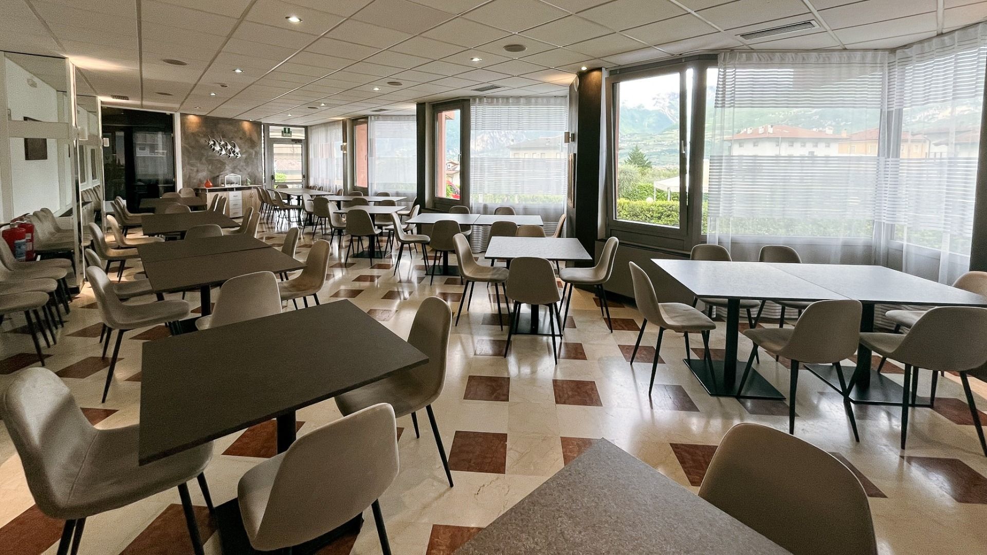 Das Hotel Everest*** bietet einen modernen, leeren Speisesaal mit quadratischen Tischen, beigen Stühlen, karierten Marmorböden, großen Fenstern mit transparenten Vorhängen und viel natürlichem Licht - ideal zum Entspannen nach einem Spiel auf dem nahe gel